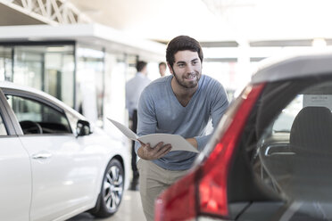 Smiling man looking at new car at car dealership - ZEF006938