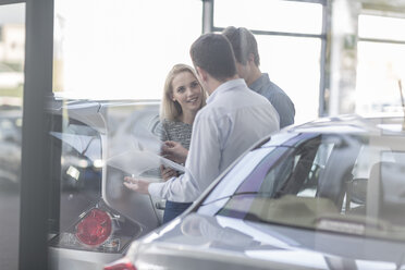 Car dealer showing brochure to young couple in showroom - ZEF006955