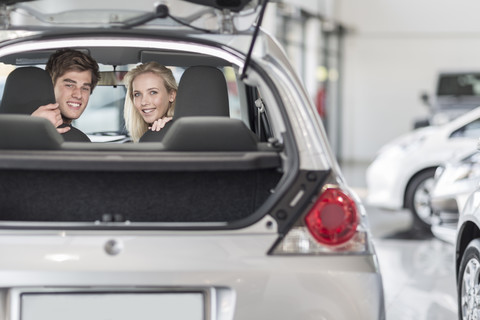 Junges Paar sitzt in einem neuen Auto im Autohaus, lizenzfreies Stockfoto