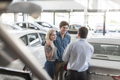 Car dealer talking to young couple in showroom stock photo