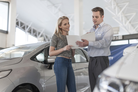 Autohändler erklärt einer jungen Frau ein neues Auto, lizenzfreies Stockfoto