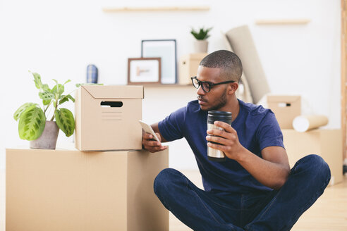 Junger Mann sitzt neben Kartons und macht eine Kaffeepause - EBSF000803