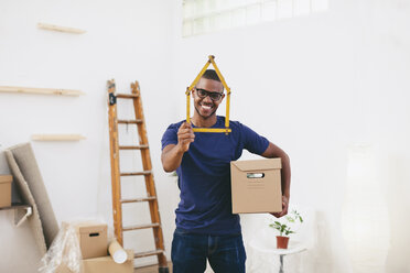 Smiling young man holding cardboard box and pocket rule shaped like a house - EBSF000811