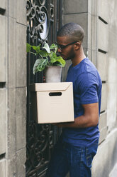 Spain, Barcelona, young man with cardboard box in front of entry door - EBSF000816