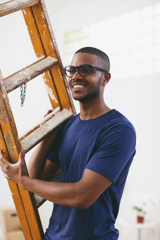 Porträt eines lächelnden jungen Mannes mit Leiter in seiner neuen Wohnung, lizenzfreies Stockfoto