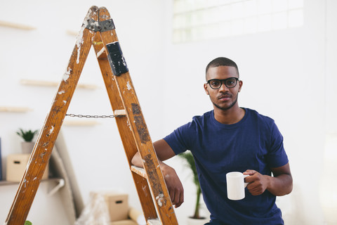 Junger Mann lehnt auf einer Stufenleiter und macht eine Kaffeepause, lizenzfreies Stockfoto