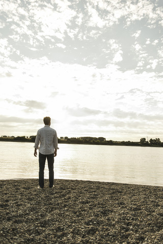 Junger Mann steht am Flussufer, lizenzfreies Stockfoto