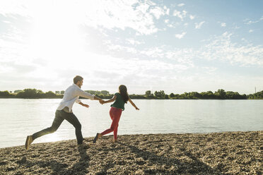 Junges Paar läuft Hand in Hand am Flussufer entlang - UUF004993
