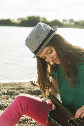 Junge Frau spielt Gitarre am Flussufer, lizenzfreies Stockfoto
