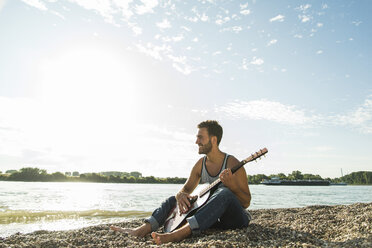 Junger Mann mit Gitarre sitzt am Flussufer - UUF005001