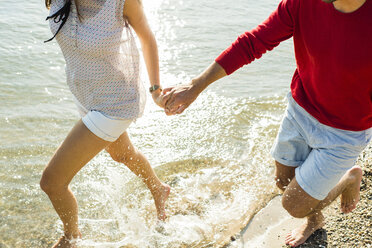 Young couple running hand in hand in a river - UUF005012