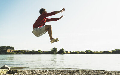 Young man jumping mid-air by the riverside - UUF005020