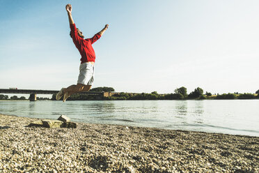 Junger Mann springt in der Luft am Flussufer - UUF005021