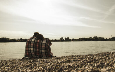 Junges Paar mit Decke zugedeckt am Flussufer sitzend - UUF005029