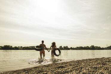 Young couple running with inner tubes in river - UUF005032