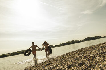 Young couple running with inner tubes in river - UUF005033