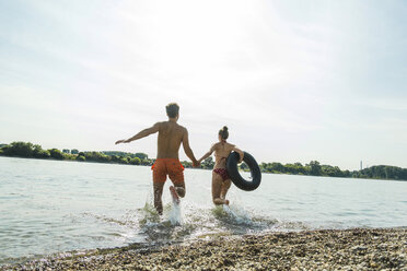 Young couple running with inner tube in river - UUF005046