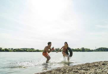Playful young couple with inner tube in river - UUF005047