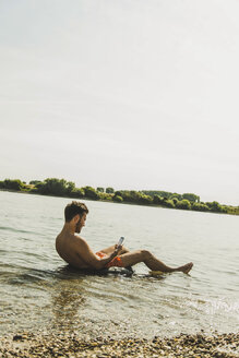 Junger Mann sitzt im Schlauchboot im Fluss und benutzt sein Smartphone - UUF005039