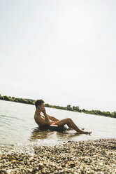 Junger Mann sitzt im Schlauchboot im Fluss und benutzt sein Smartphone - UUF005040