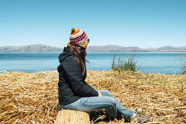 Peru, Puno, woman wearing chullo sitting on floating island in Lake Titicaca - GEMF000289