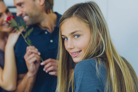 Lächelndes Mädchen mit Eltern, die eine rote Rose im Hintergrund halten, lizenzfreies Stockfoto