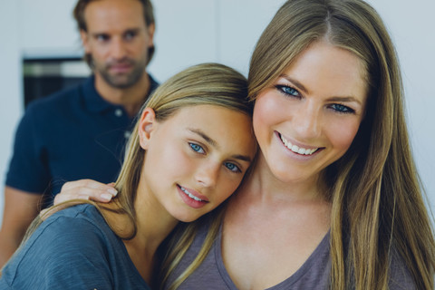 Porträt von lächelnder Mutter und Tochter mit Vater im Hintergrund, lizenzfreies Stockfoto