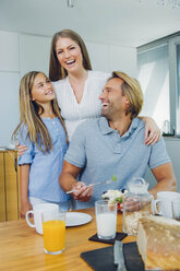 Happy mother, father and daughter at kitchen table - CHAF000864