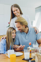 Happy mother, father and daughter at kitchen table - CHAF000865