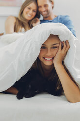 Porträt eines glücklichen Mädchens mit Welpe im Bett und Eltern im Hintergrund - CHAF000973