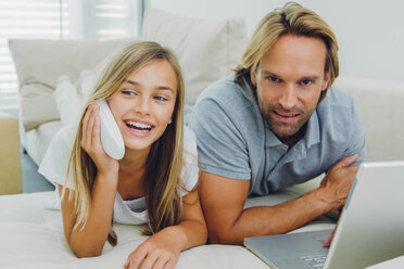 Vater und Tochter liegen auf der Couch und benutzen Laptop und Telefon - CHAF000976