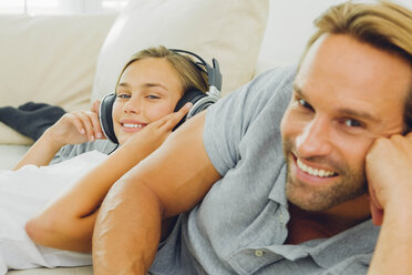 Girl lying on couch with father listening to music - CHAF000887