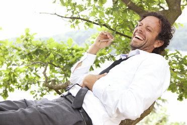Germany, relaxed businessman lying in tree smoking a joint - MFRF000262
