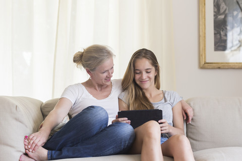 Mother and daughter sitting with digital tablet on the couch stock photo