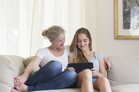 Mutter und Tochter sitzen mit digitalem Tablet auf der Couch, lizenzfreies Stockfoto