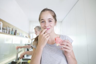 Portrait of smiling teenage girl eating melon in the kitchen - SGF001798