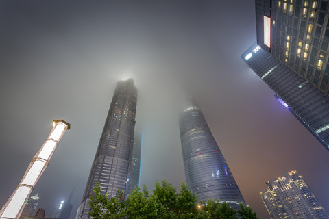 China, Shanghai, Jin Mao Building, World Financial Center und Shanghai Tower, die nachts in niedrigen Wolken hängen, lizenzfreies Stockfoto