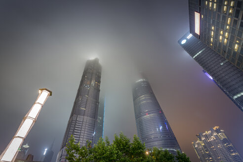 China, Shanghai, Jin Mao Building, World Financial Center and Shanghai Tower sticking in low clouds at night - NKF000326