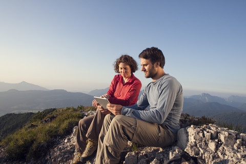 Österreich, Tirol, Unterberghorn, zwei Wanderer sitzen mit digitalem Tablet in alpiner Landschaft, lizenzfreies Stockfoto