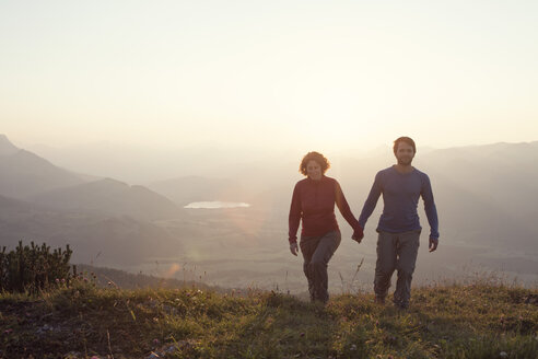 Austria, Tyrol, couple walking hand in hand at Unterberghorn at sunset - RBF002983