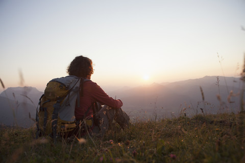 Österreich, Tirol, Unterberghorn, Wanderer rastet in alpiner Landschaft bei Sonnenuntergang, lizenzfreies Stockfoto