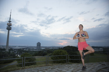 Deutschland, München, junge Frau übt morgens Yoga auf einem Hügel - FCF000704