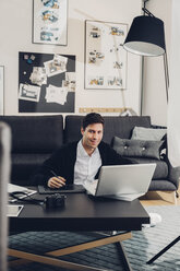 Young man in living room with laptop, digital tablet and camera - CHAF000931