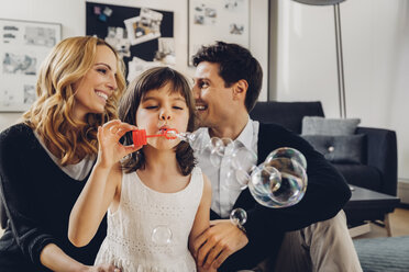 Glückliche Familie zu Hause mit einem Mädchen, das Seifenblasen bläst - CHAF000983