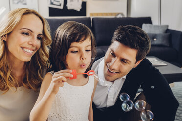 Happy family at home with girl blowing soap bubbles - CHAF000984