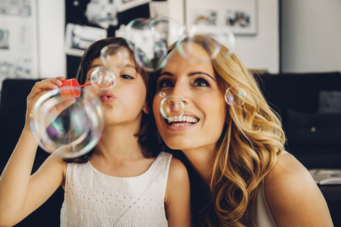 Happy mother with daughter at home blowing soap bubbles - CHAF000986