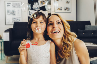 Happy mother with daughter at home blowing soap bubbles - CHAF000987