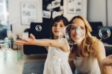 Happy mother with daughter at home blowing soap bubbles - CHAF000988