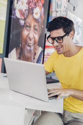 Lächelnder junger Mann am Schreibtisch mit Laptop - CHAF001041