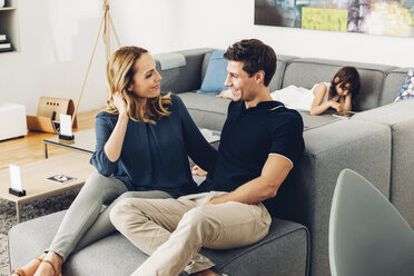 Smiling couple in living room with daughter using digital tablet in background - CHAF000998